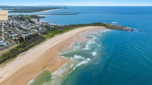 An aerial view of a coastal area with a sandy beach, a residential neighborhood, and a clear blue sea.