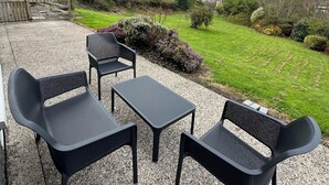 A patio area with outdoor furniture, a gravel surface, and a view of a grassy field and distant buildings.