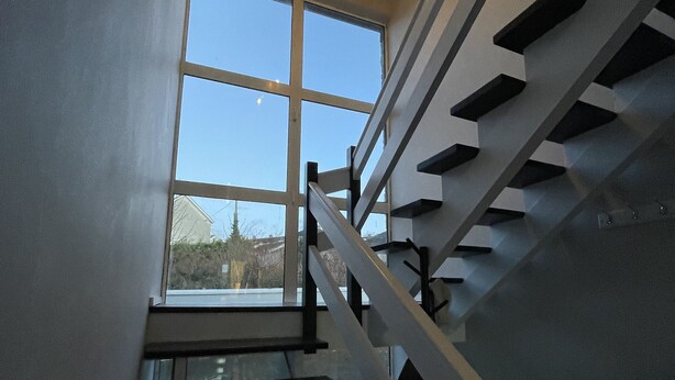 A modern staircase with a glass railing and a view of the outdoors through a large window.