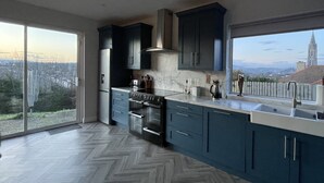 A modern kitchen with dark cabinets, a large stove, and a view of a cityscape through a sliding glass door.