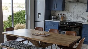 A modern kitchen with a wooden dining table, blue cabinets, and a large window.
