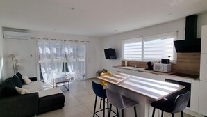 A modern kitchen with a central island, bar stools, a dining table, and a sofa. - L'eden des Aspres (Thuir)