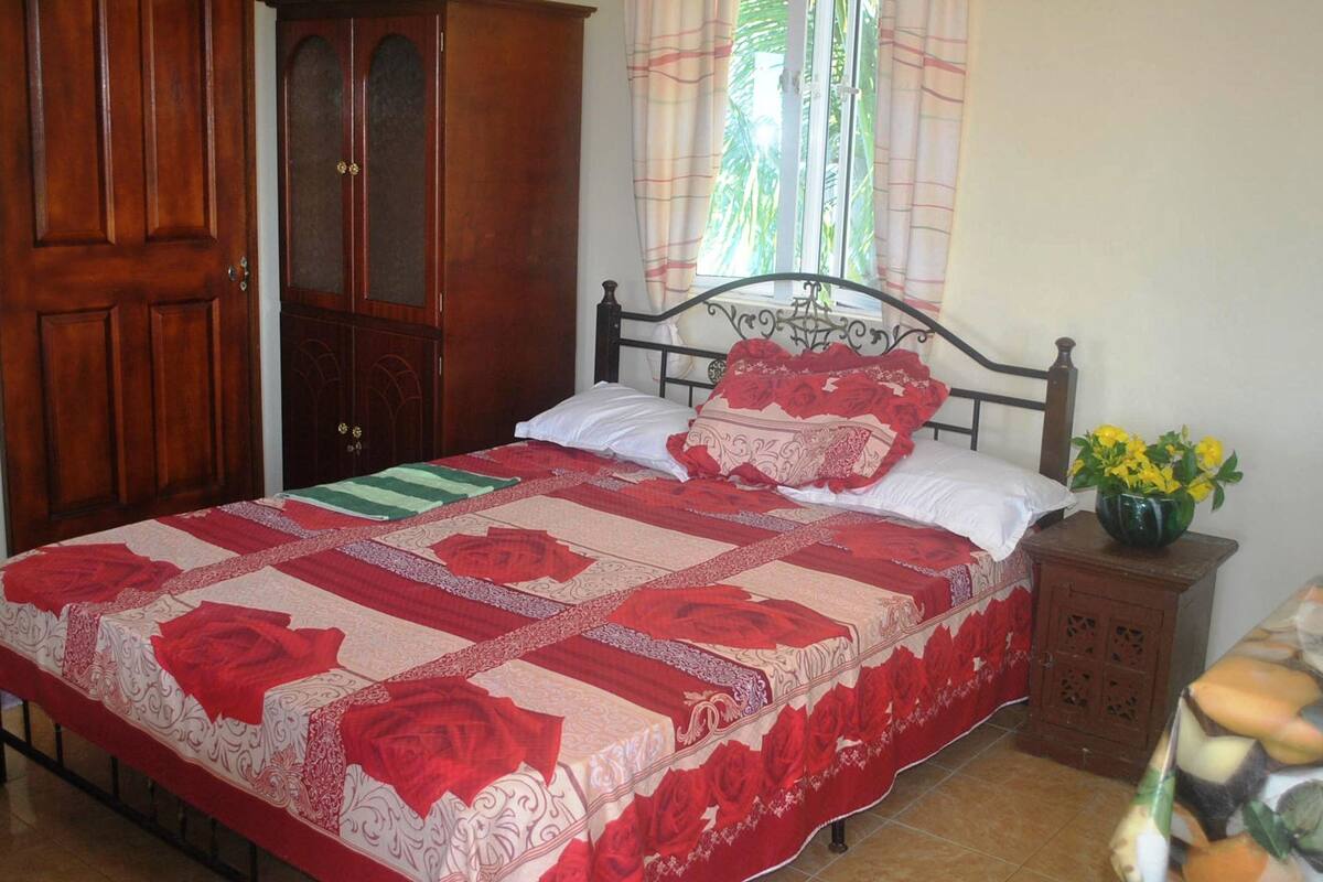 A bedroom with a bed, wooden wardrobe, and a nightstand with a vase of flowers.