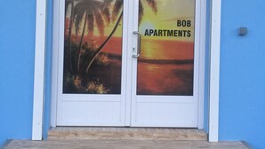A building entrance with a glass door featuring a sunset and palm tree mural, labeled "BOB APARTMENTS." - Bob Apartments (Calodyne)