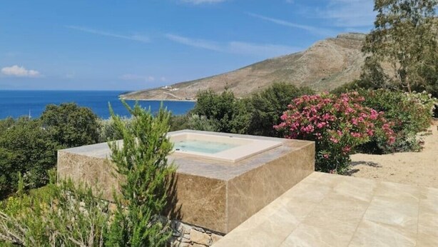 A spa area with a hot tub, surrounded by greenery and overlooking a coastal landscape. - Tilos Villa - Apartment Comfort (Tilos)