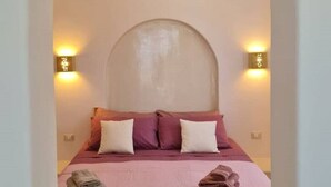 A bedroom with a large bed, two wall-mounted lights, and a unique arched ceiling. - Tilos Villa - Apartment Comfort (Tilos)