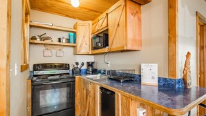 A compact kitchen with wooden cabinets, a stove, a microwave, and a sink.