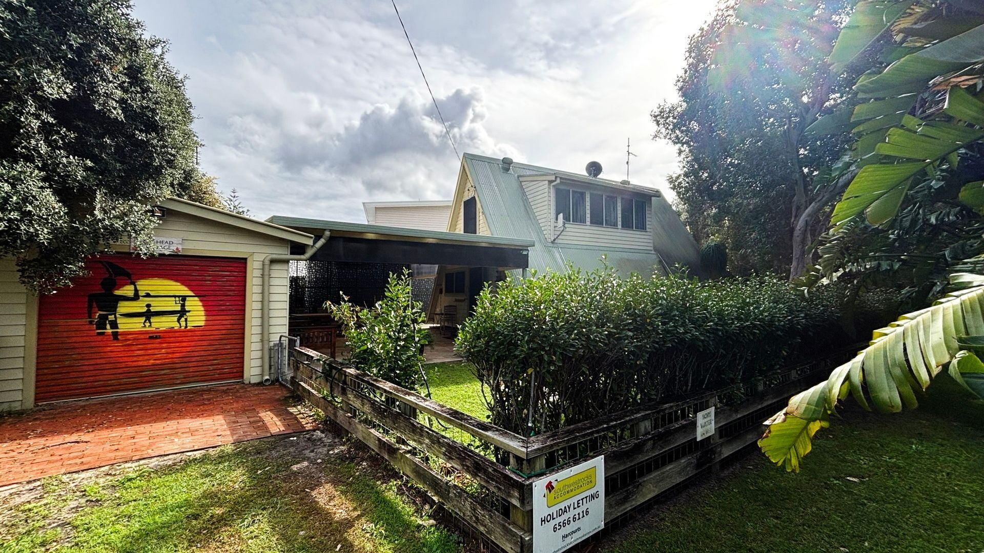 A residential property with a garage, a covered outdoor area, and a sign indicating holiday lettings.