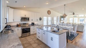 A spacious kitchen with white cabinets, stainless steel appliances, and a large island. - Sun Realty gorgeous Nags Head home across the street from Jockey's Ridge (Nags Head)