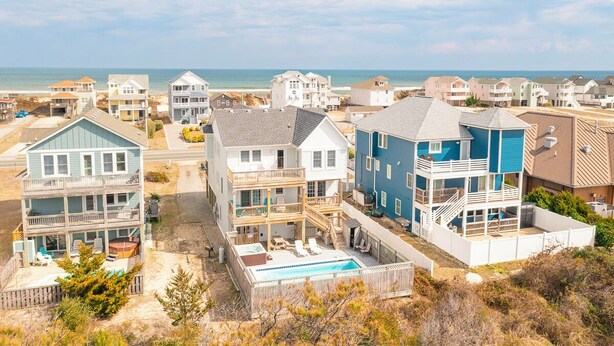 A coastal residential area with multiple two-story houses, a swimming pool, and a beach in the background. - Sun Realty gorgeous Nags Head home across the street from Jockey's Ridge (Nags Head)