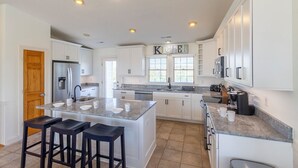 A modern kitchen with white cabinets, a central island with stools, a built-in oven, and a coffee maker. - Sun Realty gorgeous Nags Head home across the street from Jockey's Ridge (Nags Head)