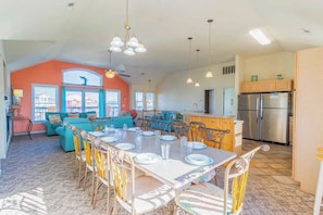 Amplia sala de estar con una mesa de comedor para cuatro, una cocina equipada con electrodomésticos modernos y una pared de acento de color naranja brillante.