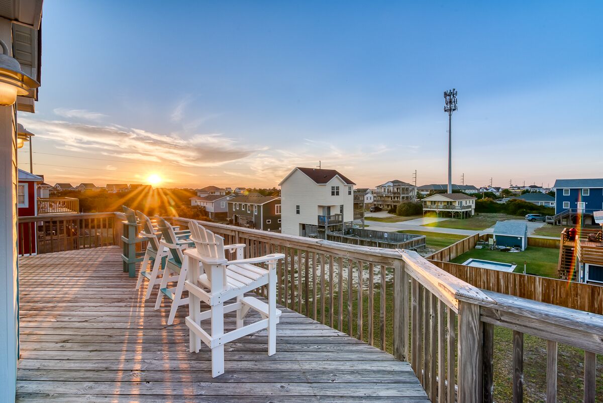 A wooden deck with chairs, a view of houses, and a sunset.