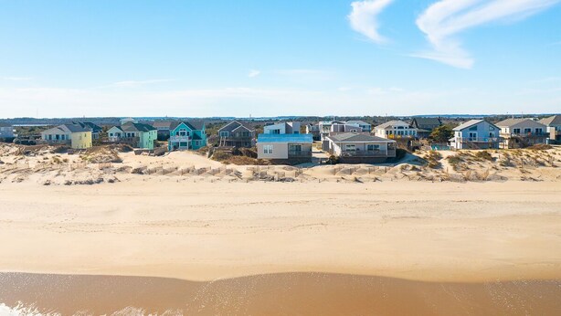 En ejendom ved stranden med huse, sandstrand og bølger.
