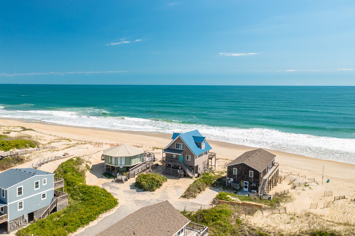 A beachfront property with multiple buildings, including a house with a blue roof and a beach house with a stone facade.