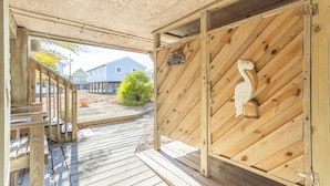 Un pontile in legno conduce a una zona riparata, con una porta in legno, una scultura di uccello e vista su case sullo sfondo.