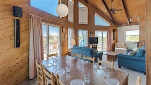 A wooden cabin with a dining area, living room, and large windows. - Oceanside Home Just a Short Walk or Bike Ride to the Beach, Shops, and Dining! (Corolla)