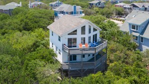 A coastal house with a balcony, surrounded by dense greenery and other houses. - Oceanside Home Just a Short Walk or Bike Ride to the Beach, Shops, and Dining! (Corolla)
