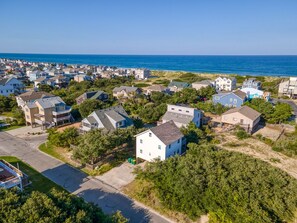 An aerial view of a coastal residential area with houses, a clear sky, and the ocean in the background.