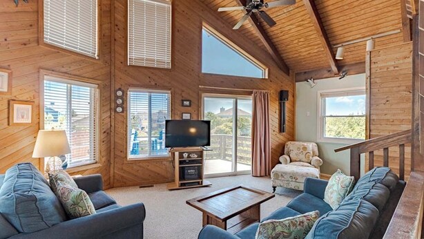 A wooden cabin interior with a TV, sofas, a coffee table, and a balcony with a view. - Oceanside Home Just a Short Walk or Bike Ride to the Beach, Shops, and Dining! (Corolla)