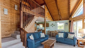 A wooden interior with a staircase, two blue sofas, a coffee table, and a dining area. - Oceanside Home Just a Short Walk or Bike Ride to the Beach, Shops, and Dining! (Corolla)