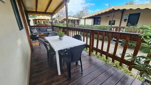 A covered outdoor area with a wooden deck, a white table, and black chairs. - Mobile Home Roma, Camping Paradiso, Viareggio, (Viareggio)