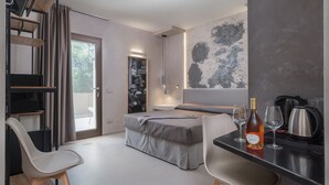 A modern hotel room with a bed, a desk, a chair, a coffee machine, and a bottle of wine.