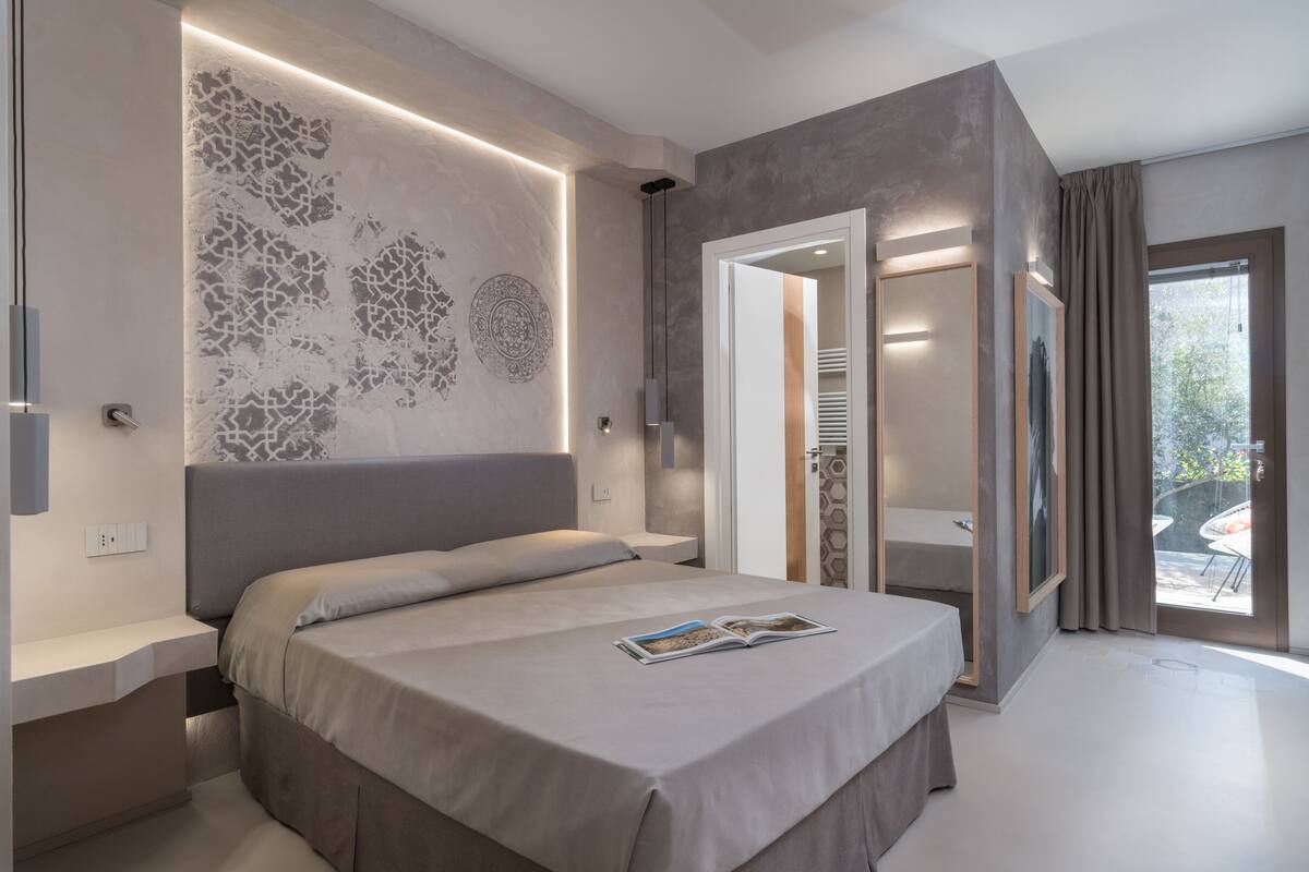 Een moderne slaapkamer met een groot bed, een nachtkastje, een wandlamp en uitzicht naar buiten.