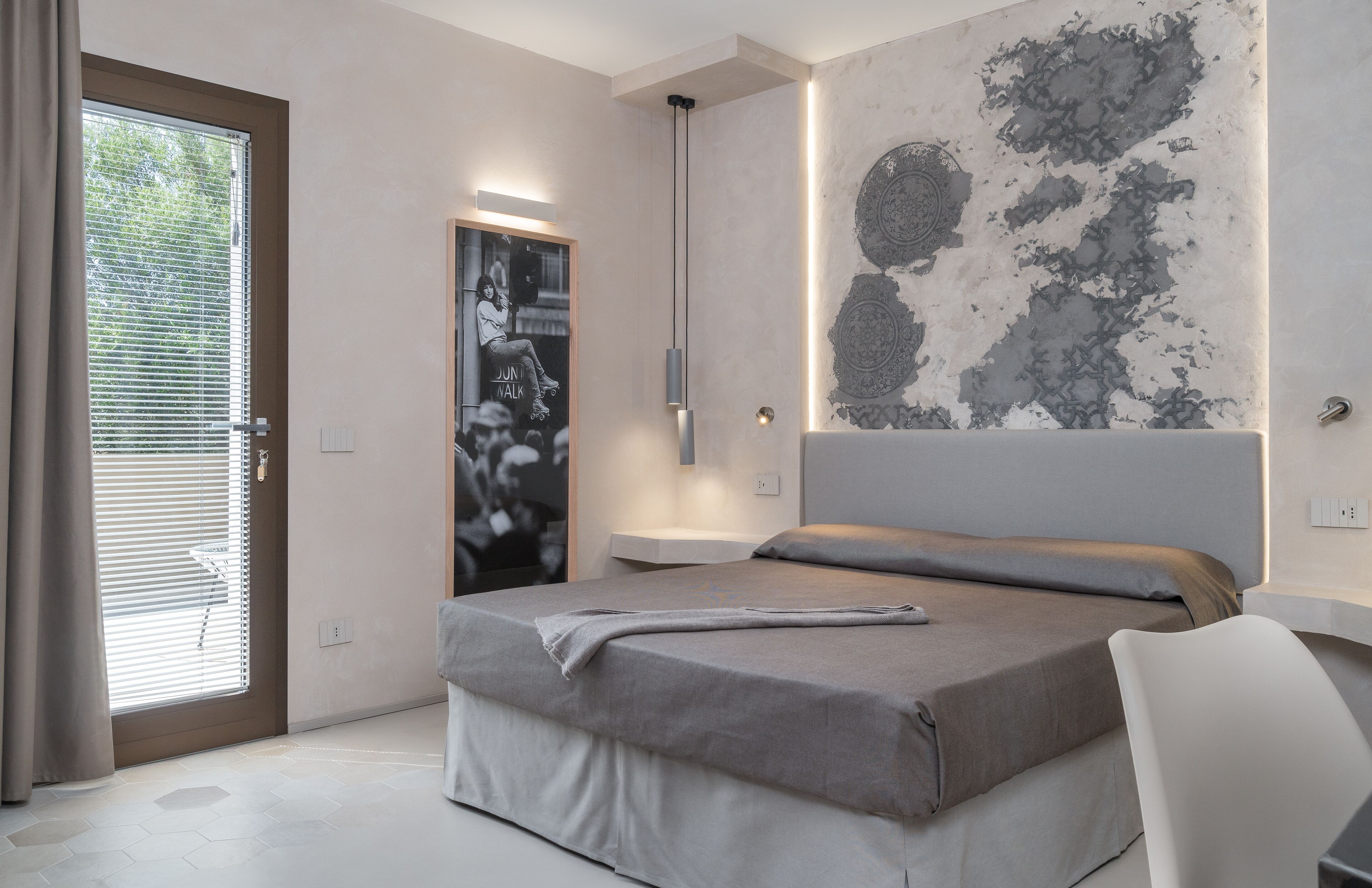 A modern bedroom with a bed, a chair, a nightstand, and a wall with a textured design.
