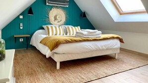 Une chambre avec un plafond en pente, un puits de lumière, un lit avec une literie blanche et des oreillers à rayures, un mur d’accent de couleur turquoise et une petite table de chevet avec une lampe.