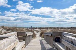 A wooden boardwalk leading to a beach with a sign indicating a parking area.