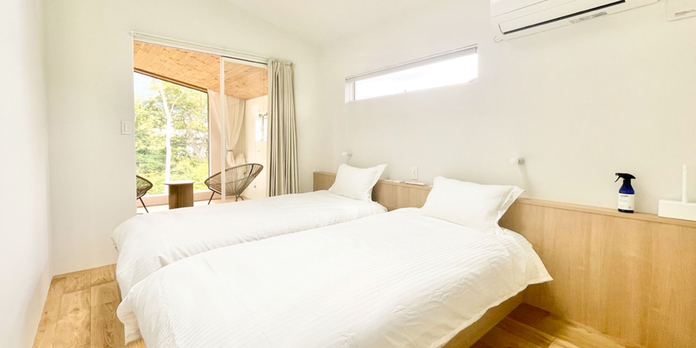 Un dormitorio con dos camas, una silla, un ventanal y un ventilador de techo.