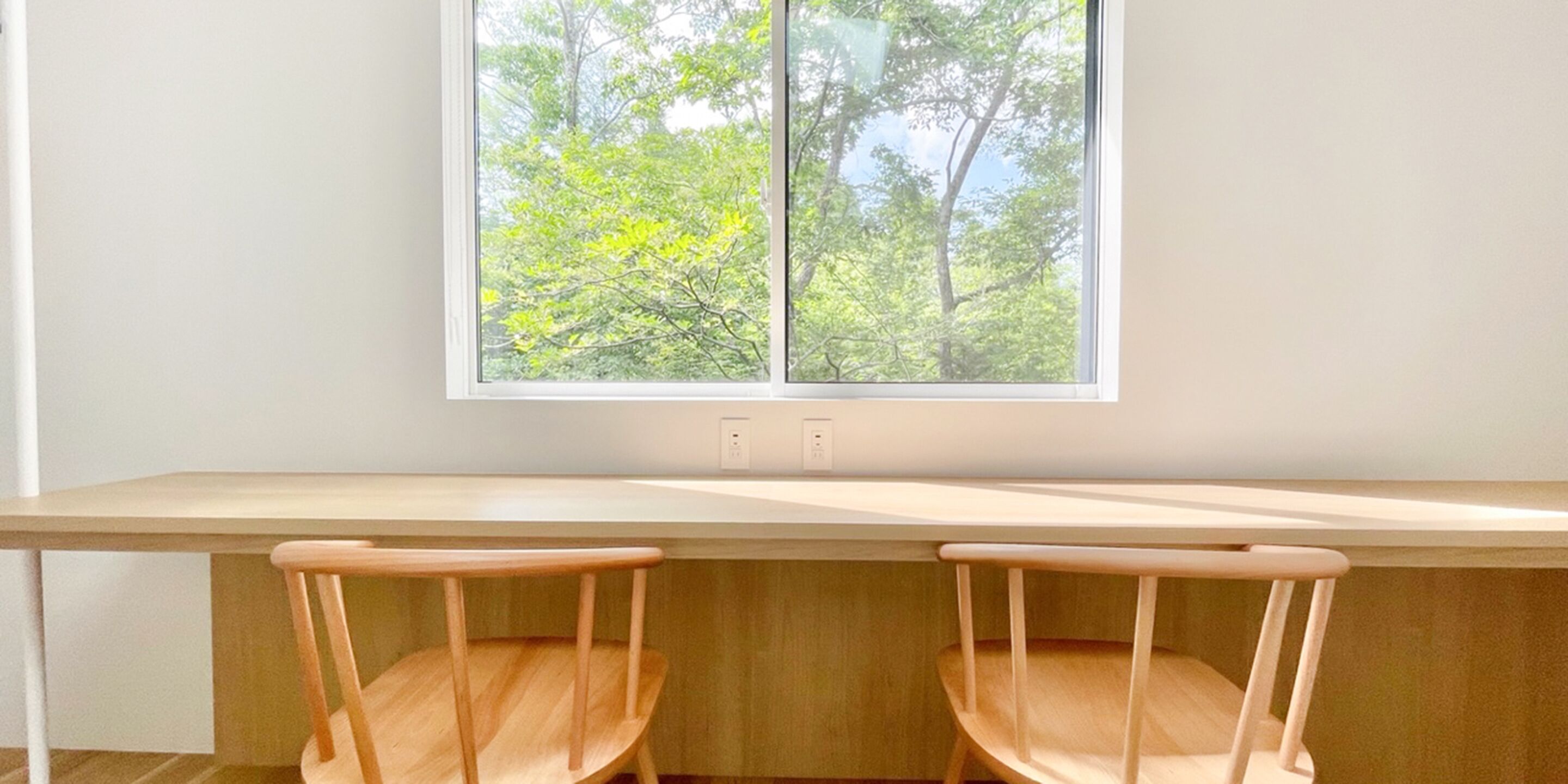 A room with a long wooden desk and two wooden chairs.