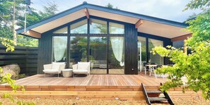 A modern house with a wooden deck, glass doors, and outdoor seating. - KARUIZAWAHOUSE VILLA (Karuizawa)