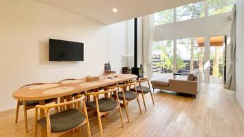 Een moderne woonkamer met een houten eettafel, stoelen, een bank en een flatscreen televisie aan de muur.