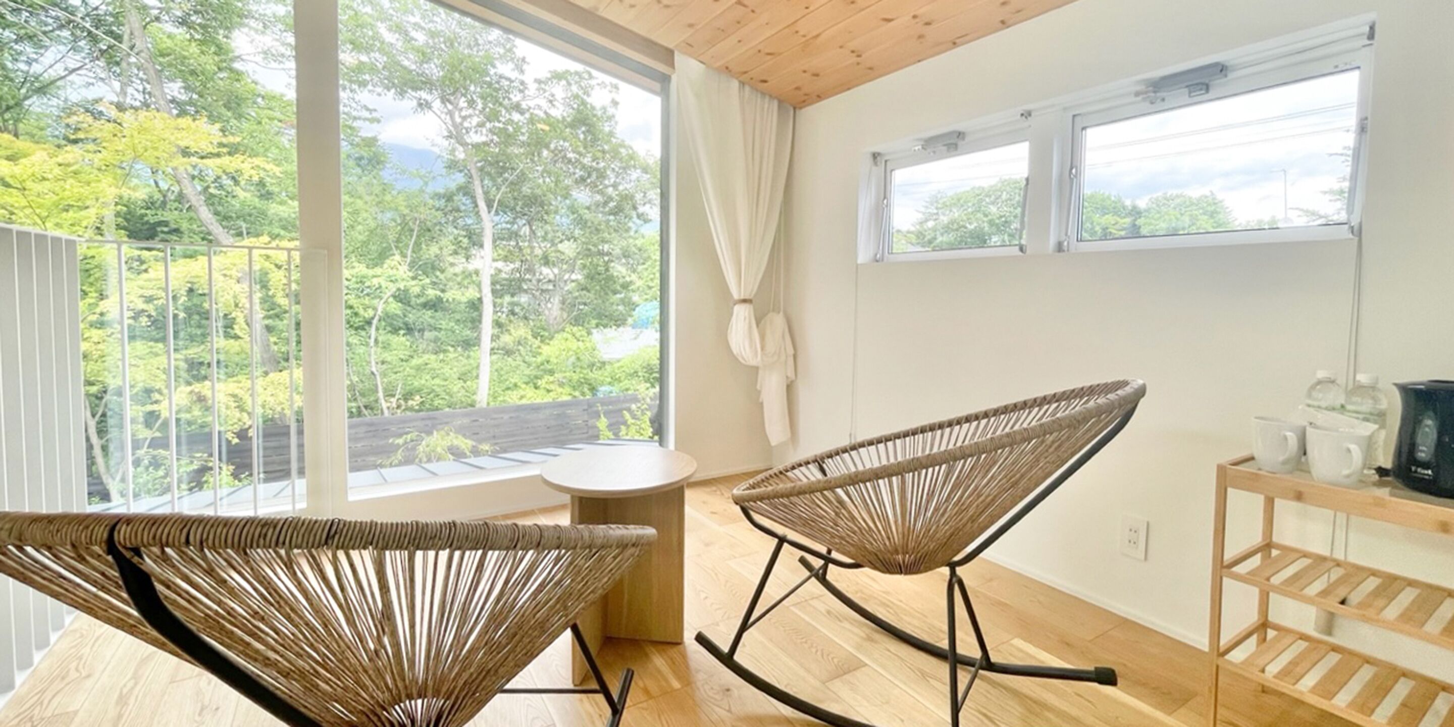 Une pièce comprenant deux fauteuils à bascule en osier, une petite table ronde et une étagère en bois sur laquelle sont posés divers objets.