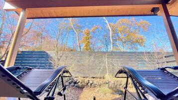 Relax in a shaded retreat with two comfortable lounge chairs under a pergola, surrounded by a serene natural landscape.
