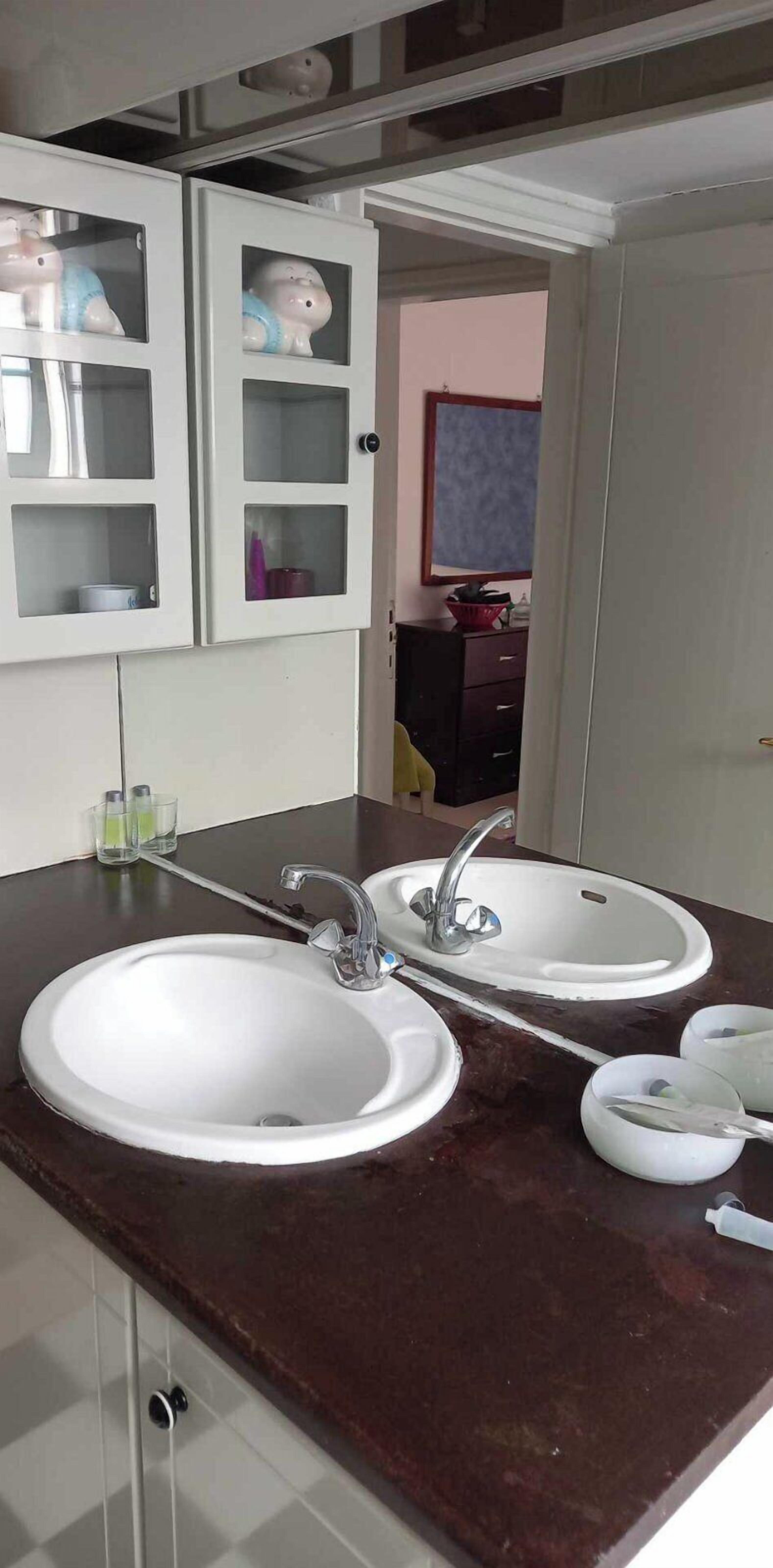 A bathroom with two sinks, a mirror, and a cabinet with glass doors.