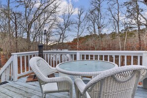 Une terrasse dotée de chaises en osier et d’une table à plateau en verre, entourée d’une balustrade blanche et d’arbres.