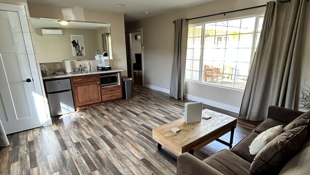A modern living room with a wooden floor, a sofa, a coffee table, and a kitchen area in the background. - The Rellik House and Winery (Central Point)