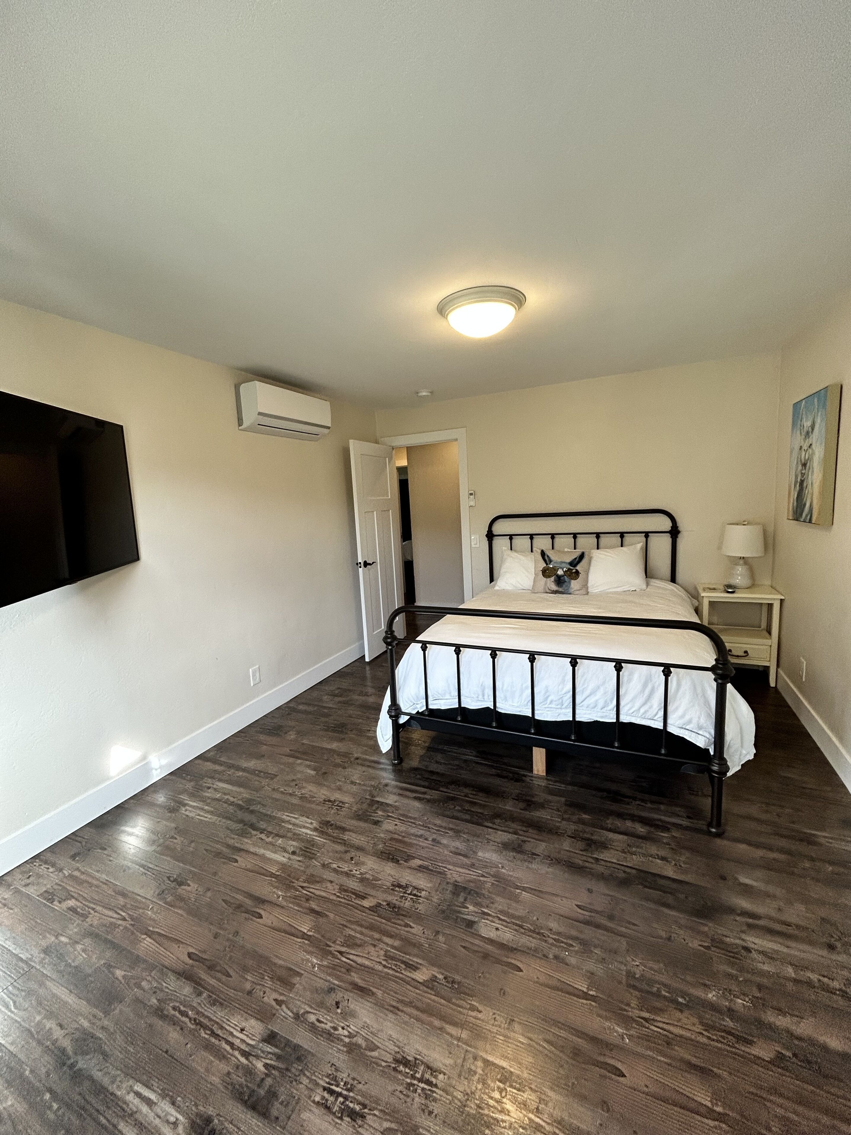 Un dormitorio con cama, mesita de noche, televisor montado en la pared y aire acondicionado.
