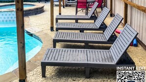 En pergola av trä med en pool och solstolar.