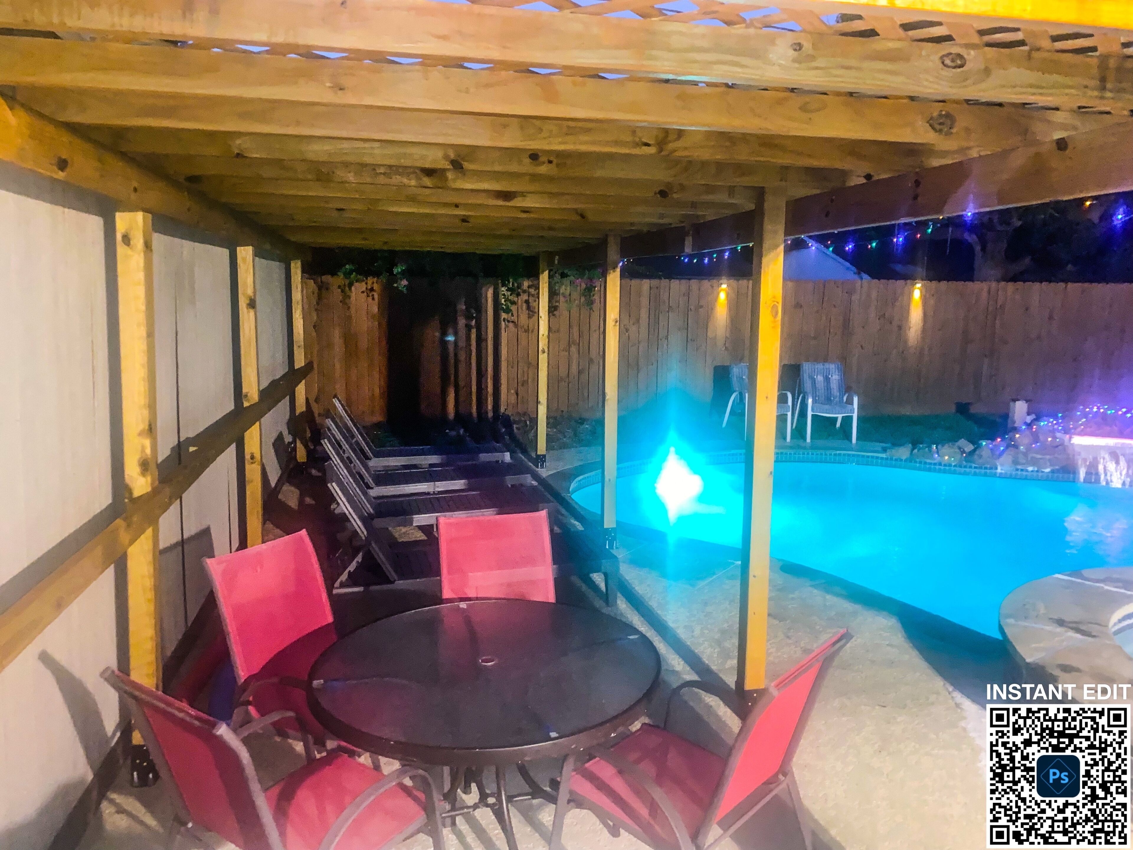 Een terras buiten met een zwembad, een houten pergola en rode stoelen.