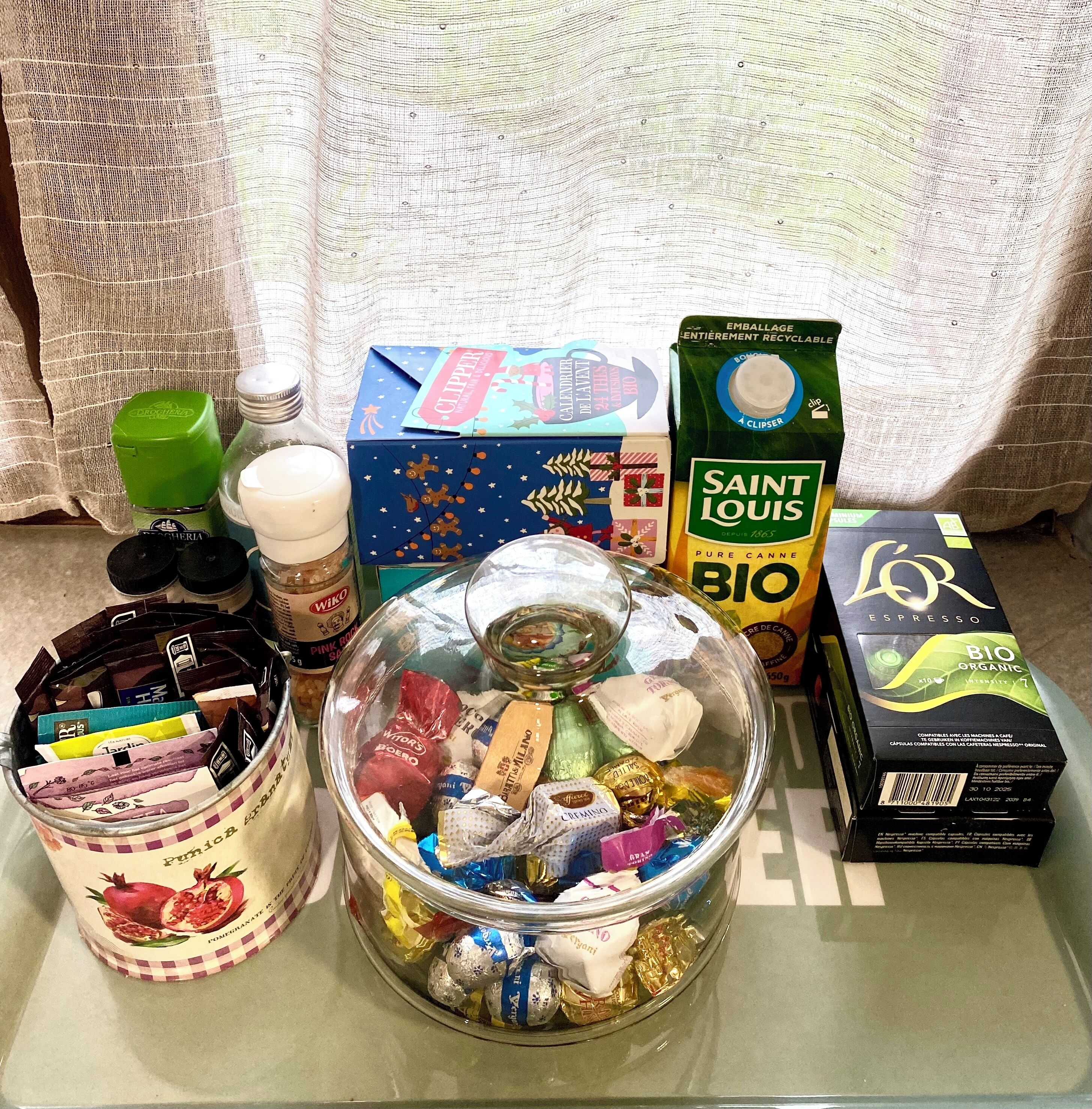 Ett urval av matvaror och drycker står uppradade på ett bord, bland annat en förpackning Saint Louis Bio-kaffe, en kartong med ekologisk mjölk och en burk med ett sortiment av chokladpraliner.