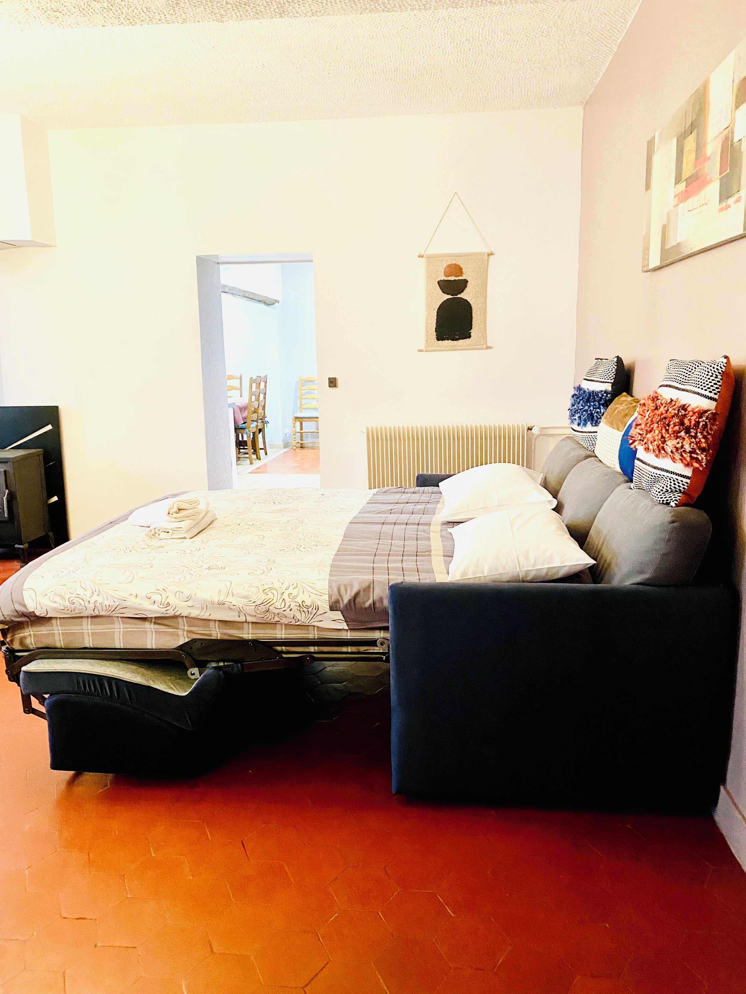 A bedroom with a bed, a sofa, a radiator, and a wall with a picture.