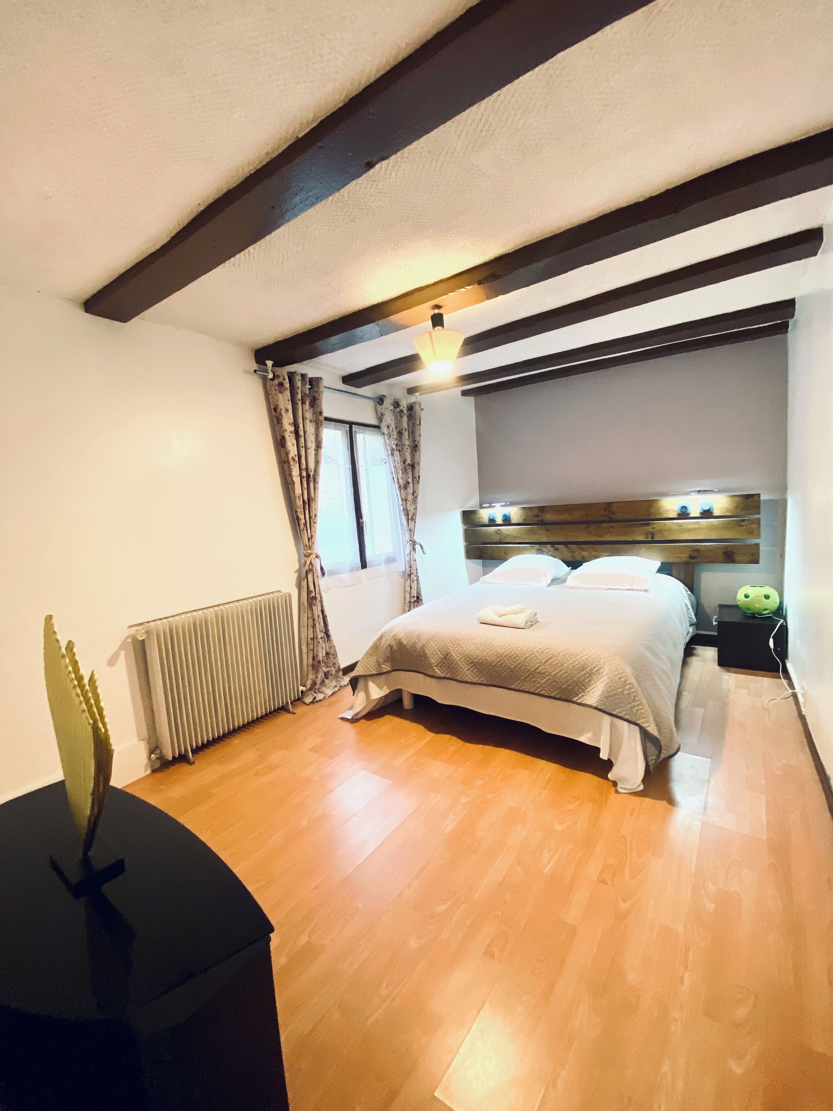 Ein Schlafzimmer mit Bett, Holzboden, Heizkörper, Vorhängen und einem Nachttisch mit Lampe.