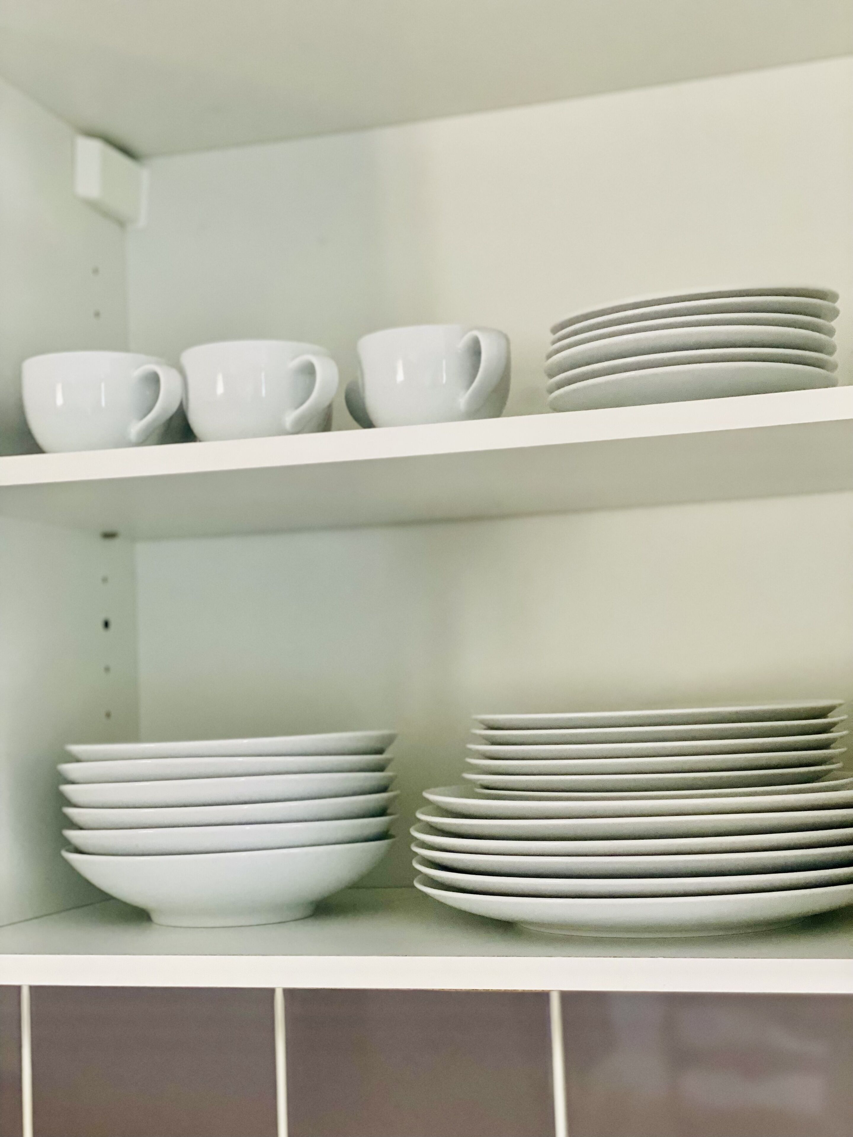 Une étagère de cuisine avec des tasses et des bols blancs.