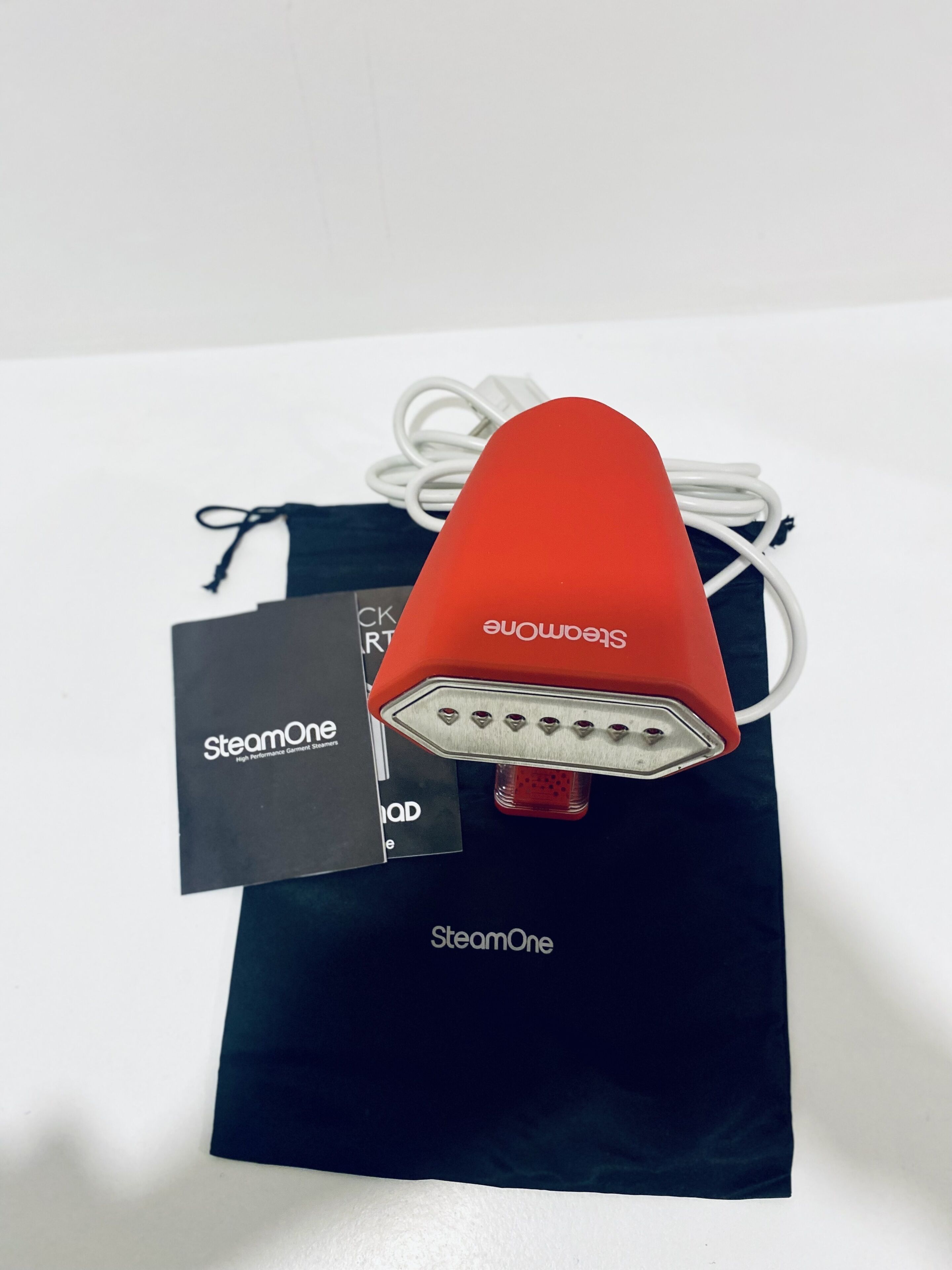 Un altaveu portàtil vermell amb un cable de càrrega blanc i una bossa negra amb el nom de marca "SteamOne" visible.