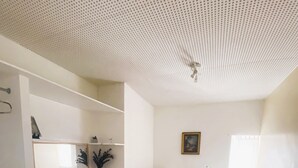 Un dormitorio con cama, mesita de noche, radiador, ventana y techo con diseño perforado.