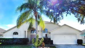 A single-story house with a garage, a small front yard with a palm tree, and a well-maintained lawn. - Family Fun 4 bedroom Vacation home (Kissimmee)